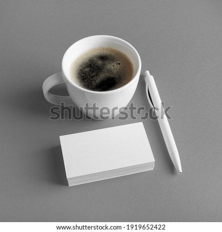 Blank business cards, coffee cup and pen on gray paper background. Brand ID set.