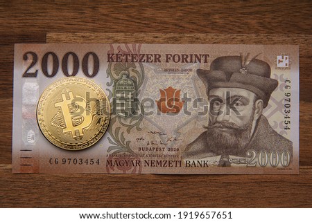 Hungarian forint 2000 forint banknote Gábor Bethlen portrait. Brown wooden table. Next to it is a gold bitcoin digital cryptocurrency coin. Bank image and photo.