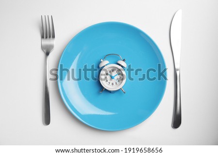 Alarm clock, plate and cutlery on white background, top view. Diet regime Royalty-Free Stock Photo #1919658656