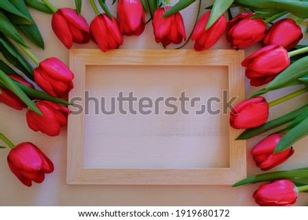 Frame of red tulips across wooden picture frame on white background. Top view. Copy space. Beauty, cosmetics, style, fashion flat lay