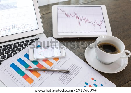 Laptop, tablet , smartphone and coffee cup with financial documents on wooden table