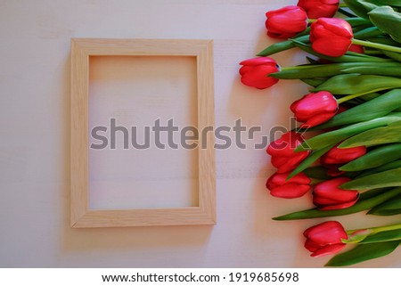 Frame of red tulips across vertical wooden picture frame on white background. Top view. Copy space. Beauty, cosmetics, style, fashion flat lay