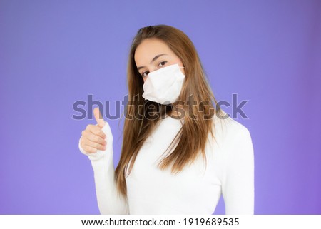Young woman wearing protective mask and showing thumb up sign. Woman wearing surgical mask for corona virus