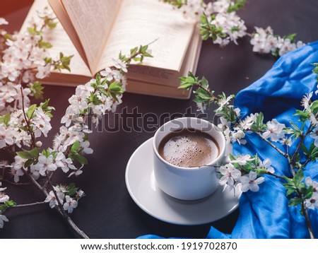 Springtime, a white cup of espresso coffee on a dark stone table, white cherry blossoms, and a book. Read a book on a weekend morning