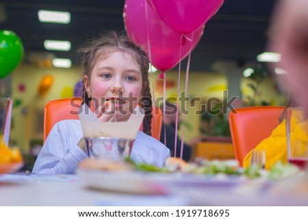 The child eats French fries in the children's restaurant. A little girl sits at a festive table on her birthday.