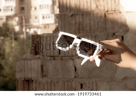 White pixel sunglasses with black lenses hold in hand closeup in a sunny day. Selective focus