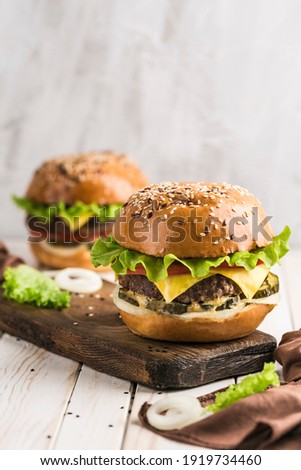 Classic burger with beef patty, cheese and fresh vegetables on a wooden board. Light background. Vertical close-up orientation with a copy space for the text.