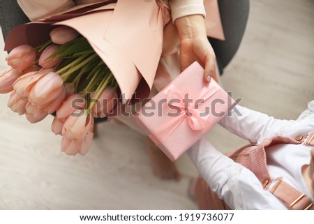 Child's hands hold beautiful pink gift box with ribbon and pink tulip flower. Top view, close-up. Preparing for the holidays.