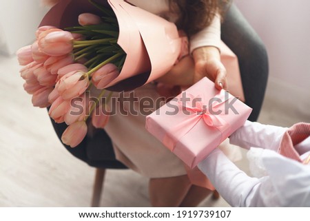 Child's hands hold beautiful pink gift box with ribbon and pink tulip flower. Top view, close-up. Preparing for the holidays.