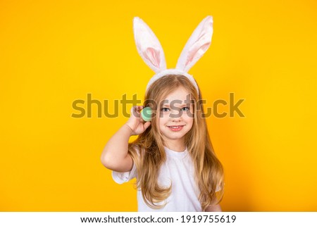 Little girl with bunny ears holds a green easter egg in her hand