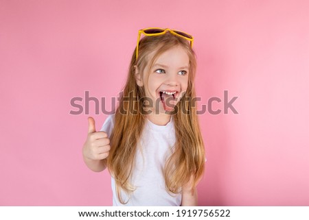 Child in sunglasses showing tongue showing cool on pink background