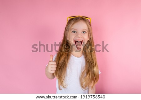 Little girl in sunglasses showing tongue showing cool on pink background