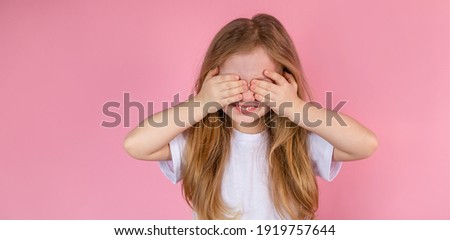 A child plays peek-a-boo on a pink background