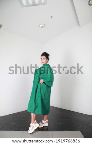 Attractive plus size brunette female model in green summer silk dress posing indoors, studio with white wall background. Catalog fashion shooting of overweight woman in clothes. Body positive concept