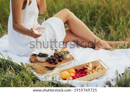 Cropped picture of girls is having picnic on a grass in the park with  wine, cheese and fresh fruits.