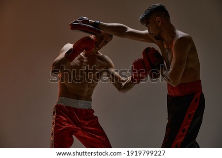 Fighting guys during mixed fight workout. Athletic males in boxing gloves training martial arts technique
