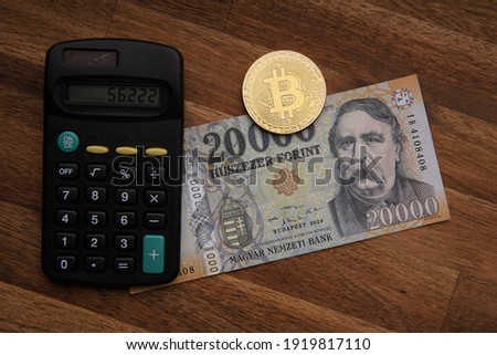Hungarian forint 20 000 forint banknote Ferenc Deák. Calculator on brown wooden table. Next to it is a gold bitcoin digital cryptocurrency coin and paper money. Bank image and photo.