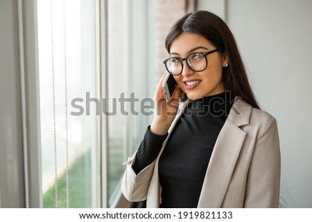 beautiful young woman in office with cellphone wearing glasses 