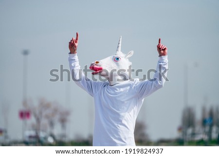 Man wearing unicorn mask making finger gesture pointing up