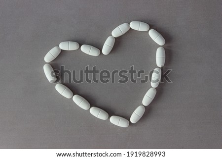The capsules are laid out in the shape of a heart on a gray background.