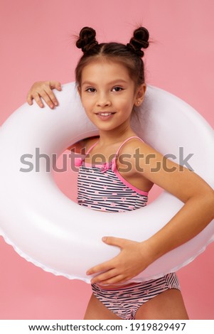 cute little child girl in swimwear with white rubber circle on pink background