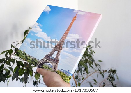 Canvas print stretched on frame with gallery wrap, hand holds travel photography, photo printed on canvas in white wall room with green houseplant, side view