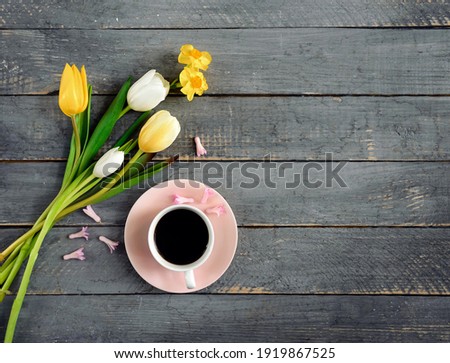 A coffee cup with yellow tulips on wooden background. Flat lay, top view. Concept of holiday, birthday, Easter, March 8