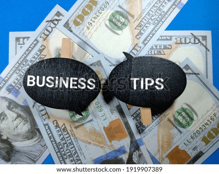 Selective focus.Word BUSINESS TIPS on wooden board with dollar banknote on blue background.Business concept.Shot were noise and film grain.