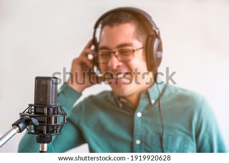 Portrait of a young man, running a podcast live from his home. He has headphones