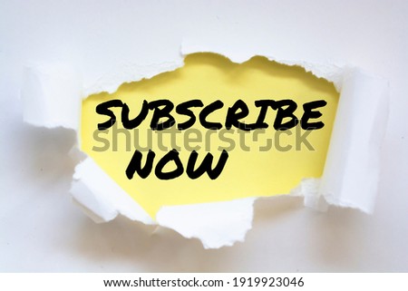 Text SUBSCRIBE NOW appearing behind torn white paper. Top view.