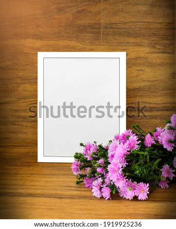 A white blank photo frame with a bouquet of flowers in front of wooden wall