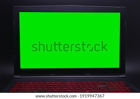 Photo of black laptop and red color keyboard with green screen for edit. Isolated on black background.