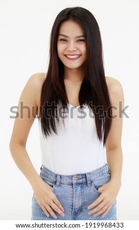 Portrait of One Asian adult woman with long black hair standing, smiling and looking at a camera with hands in blue jean. Woman wear a white camisole and jeans shoot with white background in a Studio.