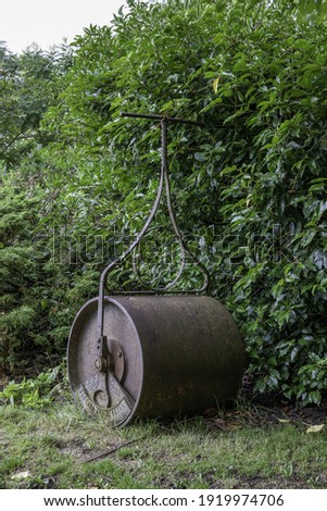 A vertical shot of an old and rustic cricket pitch roller with green leaves in the background