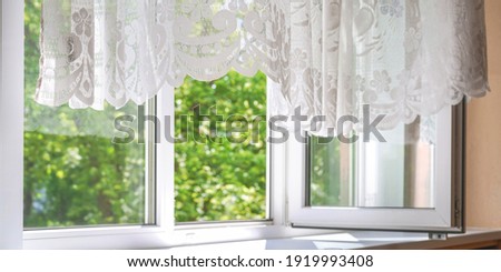 windows and lacy curtains of white colours against blurry green garden trees under bright sunlight on summer day Royalty-Free Stock Photo #1919993408