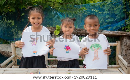 Cute preschooler boy and girl  showing his drawing on paper, Active 4-5 years kid with proud face holding his painting bee on field for his school homework