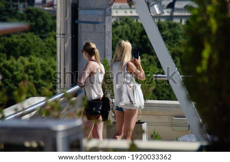 A back view of two young blonde girls wearing shorts standing outdoors and taking photos of nature on a sunny summer day