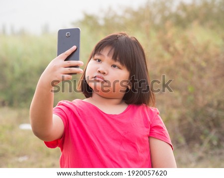 Happy portrait fat girl Asian cute cheeks with black hair wearing red-pink shirt. Taking a picture with smartphone with a bright smile In evening at sunset At the front garden with Twilight of the day