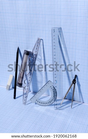 Vertical image.Pencil, rulers, t-square, protractor, eraser, measuring compass on the blue graph paper