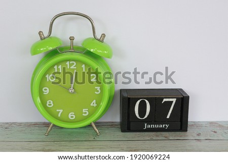 green alarm clock and cube calendar date January 7 on the table