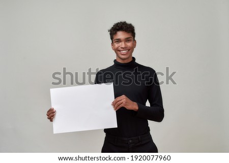 Happy young african american man holding blank bill and smiling at camera while posing on light background. Discount and sale concept