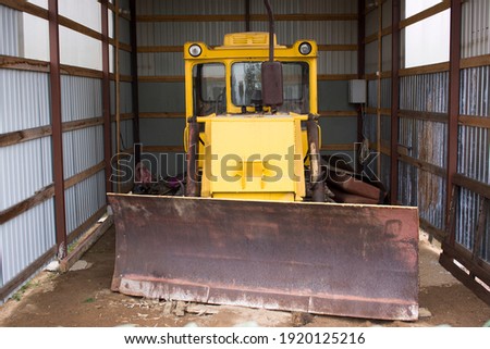 Large powerful yellow tractor with large wheels in the hangar, warehouse, garage with open gates