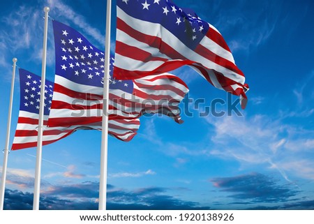 three Flags of United States of America being waved in the breeze against a sunset sky. US flag