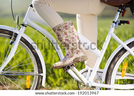 Detail of young woman's feet in boots riding on bike in green field