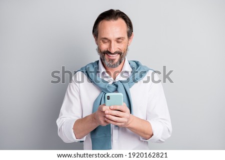 Photo of good mood mature guy dressed white shirt pullover shoulders communicating modern device isolated grey color background