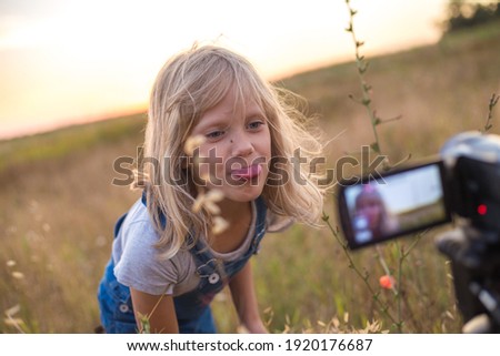 The child shows his tongue into the camera lens. Summer blonde girl plays in the meadow. Carefree weekend. soft focus