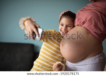 Little happy girl takes a picture of herself and her mother's belly. Focus is on stomach and little girl. 