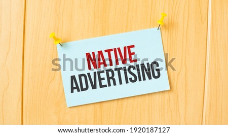 NATIVE ADVERTISING sign written on sticky note pinned on wooden wall