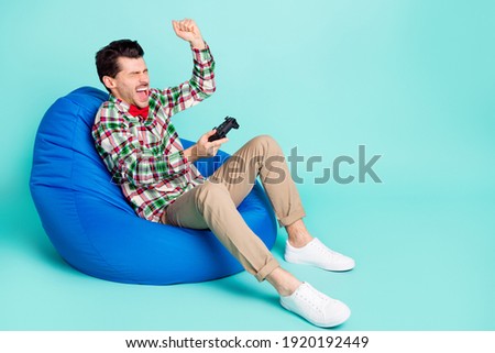 Profile photo of guy sit bag hold gamepad raise fist wear plaid shirt tie pants shoes isolated blue color background