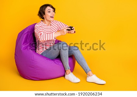 Full size photo of young happy positive good mood girl sit armchair playing playstation isolated on yellow color background